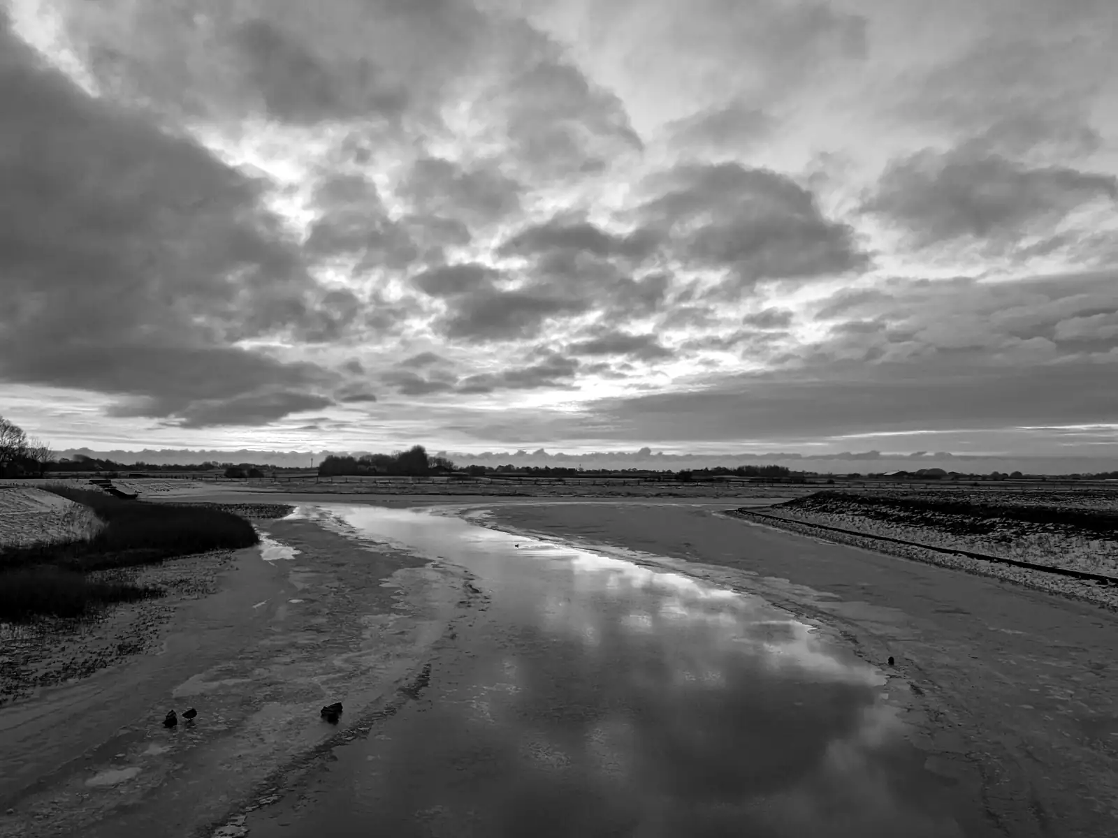 Priel im Watt bei Schnee, Wolken spiegeln sich im Wasser, schwarz-weiß – Foto: Jan Pleitner